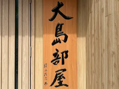 A wooden sign with Japanese characters reading 'Oshima Beya,' indicative of a sumo stable.