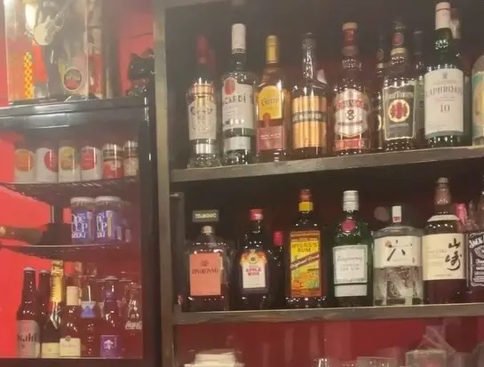 A shelf filled with various bottles of alcohol, including spirits and beer, in a cozy bar setting.