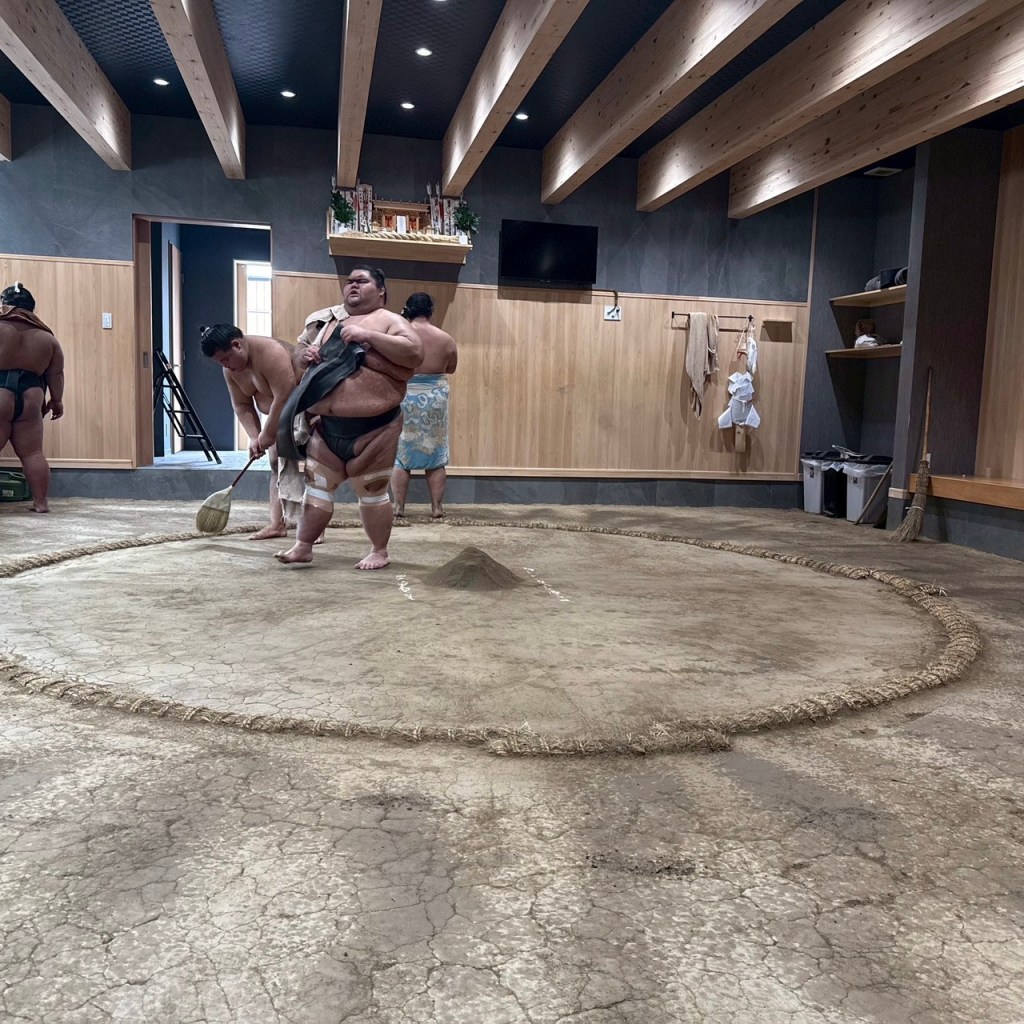 Sumo wrestlers preparing the dohyo (ring) in a training facility, showcasing traditional Japanese culture.