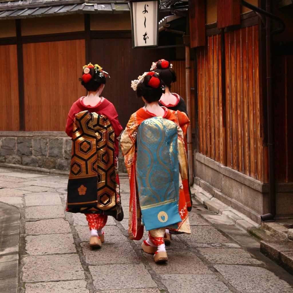 Three women in traditional Japanese kimono walking down a stone-paved street in a historic district.