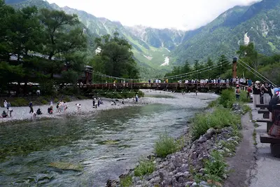 A scenic view of a river surrounded by lush greenery and mountains in Japan, with several people enjoying the landscape.