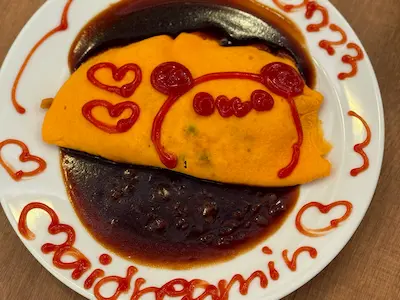 An attractive plate of omelette rice, decorated with ketchup drawings of a bear face and hearts, served on a wooden table.