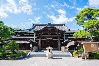 A traditional Zen temple in Japan with a wooden entrance and surrounding greenery under a blue sky.