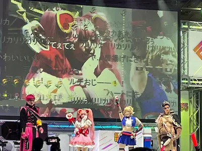 Cosplayers perform on stage with colorful costumes and animations displaying behind them.