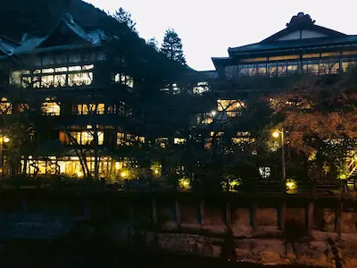 Illuminated traditional ryokan building nestled in nature during dusk.