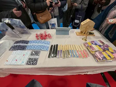 テーブルの上に並べられた様々な和風のアイテム。色とりどりの布製品、赤い飴、箸、そして木製の小物入れが展示されている。